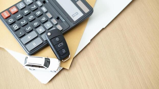 Calculator, key fob, and a white toy vehicle on a wooden desk representing transportation budget planning